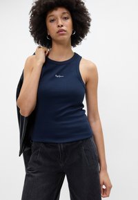 Navy ribbet tank topp med rund halslinje, tettsittende fasong og hvit logo-detall. Stylet med svarte høytlivsbukser og en skinnjakke.