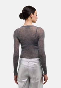 Haut à manches longues gris avec une texture transparente, associé à un pantalon métallique argenté. Le haut présente un col rond et une coupe ajustée.