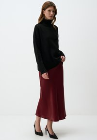Maglione nero a collo alto in maglia abbinato a una gonna midi di satin cremisi e décolleté neri a punta. Texture liscia, vestibilità rilassata, silhouette elegante.