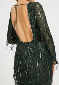 Zielona sukienka z cekinami z długimi rękawami, z głębokim, otwartym tyłem i frędzlami. Przezroczysty materiał o błyszczącej teksturze i eleganckim wzorze.