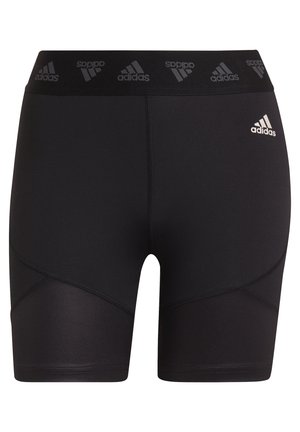 Osoba nosząca czarne, sportowe szorty Adidas z wysokim stanem i czarne buty biegowe Adidas, stojąca z nogami lekko rozstawionymi na białym tle.