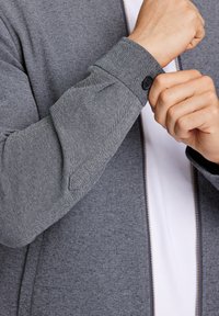 Grå zip-up jacka med ett strukturerat, vävt tyg, detalj med knappad mudd och ett slätt innerfoder.