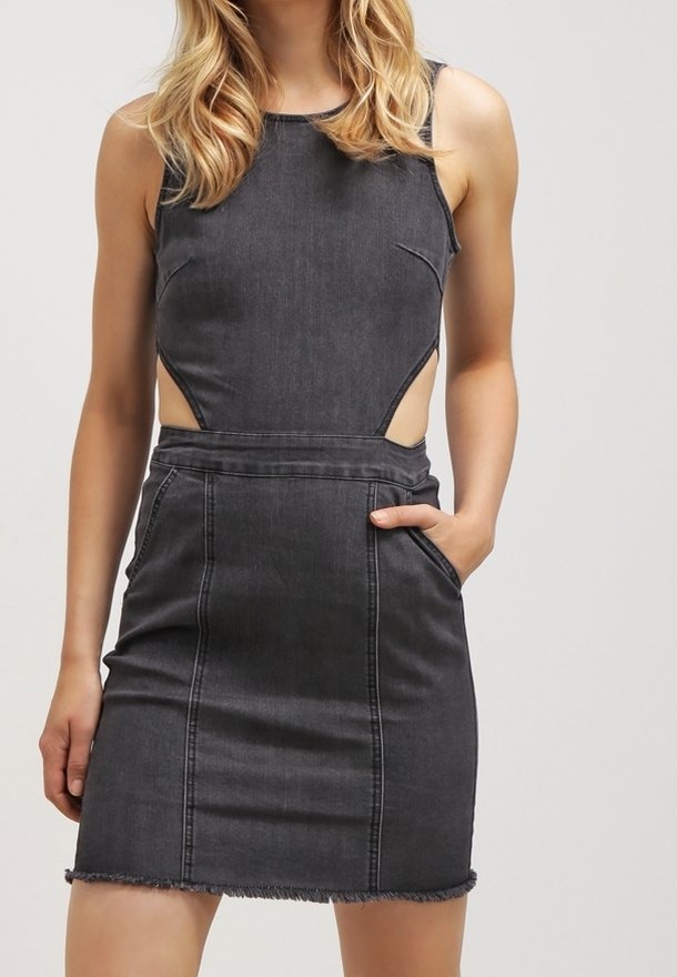 Robe en jean gris foncé sans manches avec découpes latérales, poches avant et ourlet effiloché portée par une personne aux cheveux blonds sur fond uni.
