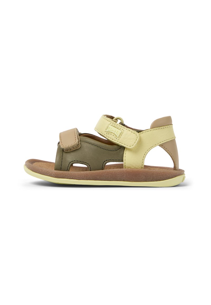 Ruskea ja keltainen nahkasandaali, jossa on säädettävät hihnat, avoin sivumuotoilu ja teksturoitu luonnonpuupohja. Kevyt kumipohja.