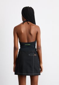 Top nero con scollo a halter e scritta verde "SANTA CRUZ", abbinato a una gonna nera con cuciture bianche e tasca posteriore.