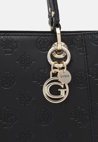 Czarna skórzana torebka z wytłoczonymi logo, złotym wykończeniem oraz zawieszką z nazwą marki "GUESS".
