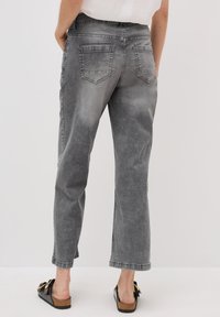 Jeans gris de corte ajustado fabricados en denim. Cuenta con cinco bolsillos, detalles de desgaste y un dobladillo en los extremos. Combinados con sandalias negras.