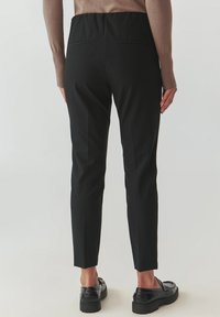 Pantaloni negri, ajustați, cu o siluetă elegantă, realizati dintr-un material neted, cu un talie înaltă și două buzunare la spate. Purtați cu pantofi negri.