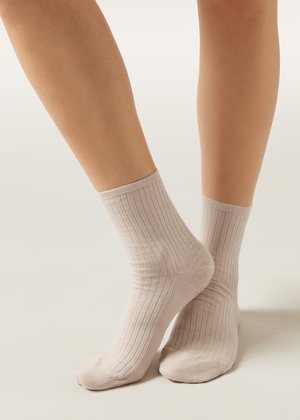 Two legs wearing light beige ribbed crew socks, one foot flat and the other slightly raised on toes against a neutral background.