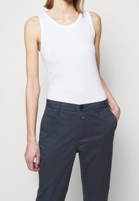 Vit ärmlös linne, figursydd design, tillverkad av ett mjukt material, kombinerad med mörka byxor med knappstängning och sidofickor.