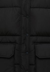 Veste matelassée noire avec panneau central à boutons-pression et deux poches avant à rabat visibles.