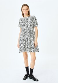 Lyhythihainen, musta-valkoinen pilkullinen mekko, jossa on kerroksellinen hame ja pyöreä kaula-aukko, valmistettu kevyestä kankaasta. Yhdistetty mustiin sukkiin ja kenkiin.