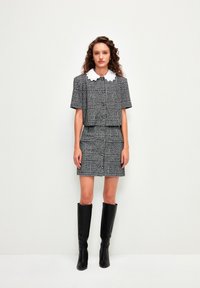 Korte mouwen zwart-wit gepatternde cropped jack met bijpassende rok, voorzien van een witte scalloped kraag en kniehoge zwarte laarzen.