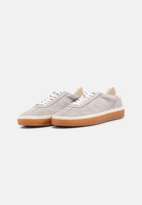 Suede sneakers i lys grå med hvite snørebånd og tunge, med en gummigummisåle. Teksturert detaljer på overdelen forbedrer designen.