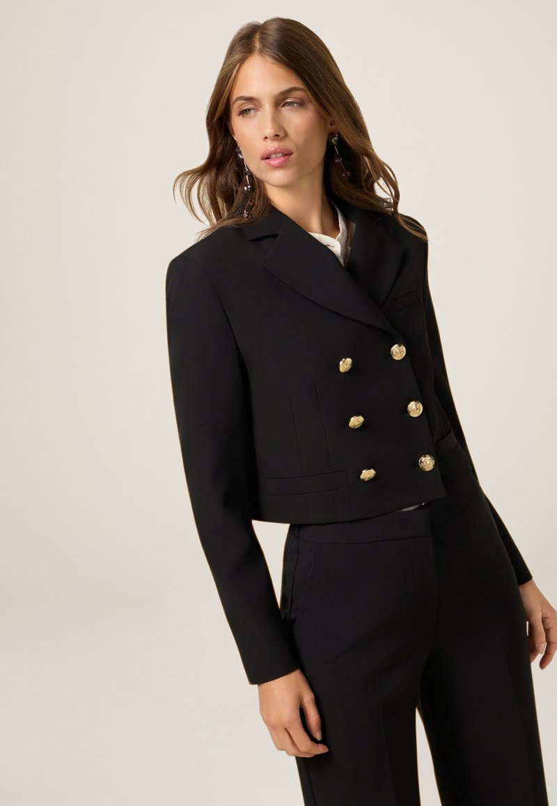 Blazer corto nero realizzato in tessuto strutturato, con un design doppiopetto caratterizzato da bottoni dorati e rever a punta.