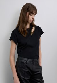 Black short-sleeve top featuring a unique cutout adorned with textured golden accents, paired with sleek black leather pants.