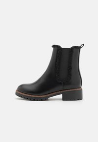 Bottines noires à talon, avec une finition en cuir lisse, des panneaux latéraux en élastique texturé et une semelle marron avec des rainures pour une meilleure adhérence.