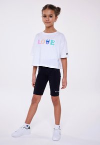 T-shirt bianco a maniche corte con grafica colorata "LOVE", abbinato a pantaloni da bicicletta neri. Sneakers bianche con dettagli verde completano l'outfit.