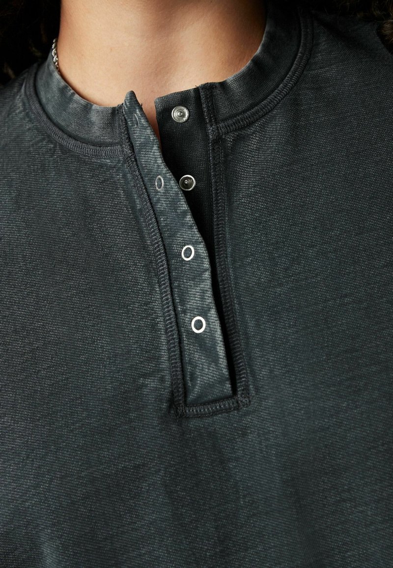 Gros plan d’une chemise gris foncé avec un tissu texturé et une patte de boutonnage pression partiellement déboutonnée au col.