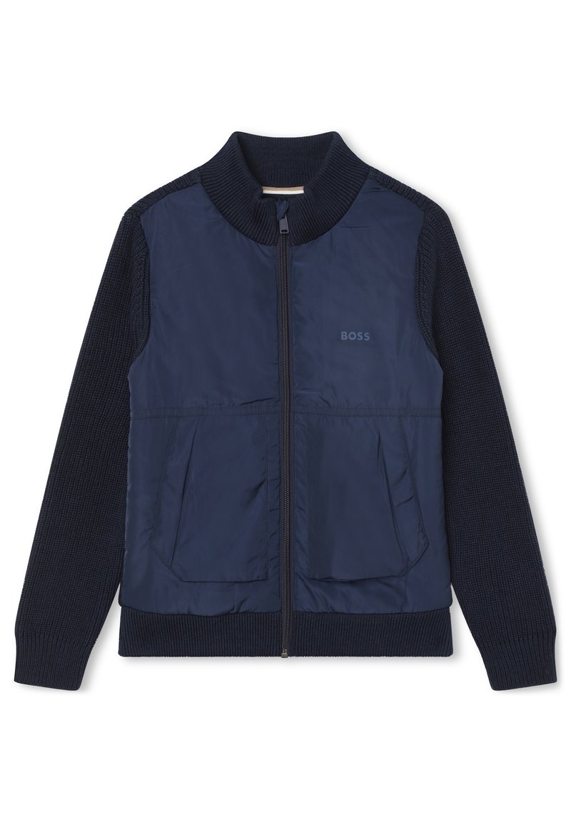 Giacca blu navy con zip frontale, maniche a maglia e due tasche frontali. Realizzata in un materiale morbido e leggero con una finitura testurizzata.