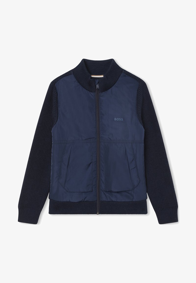 Giacca blu navy con zip frontale, maniche a maglia e due tasche frontali. Realizzata in un materiale morbido e leggero con una finitura testurizzata.