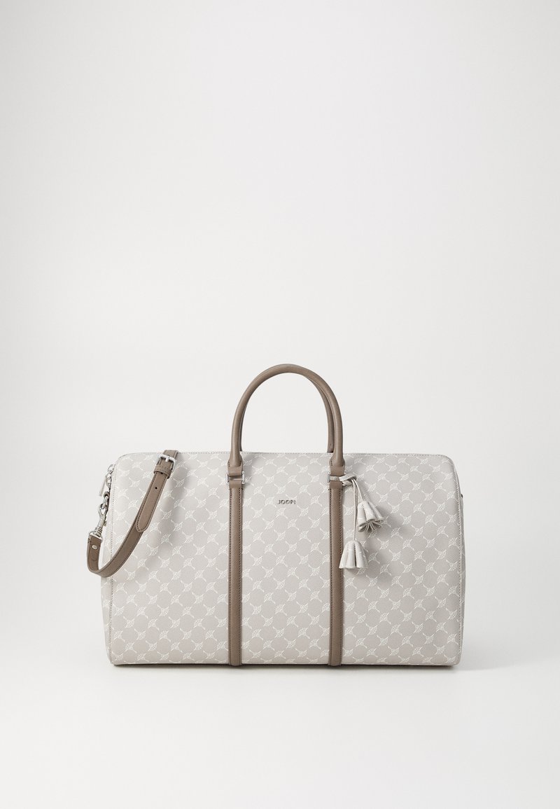 Sac de voyage gris clair avec une surface à motifs, poignées et accents en cuir marron, fermeture éclair et pampilles décoratives sur le côté.