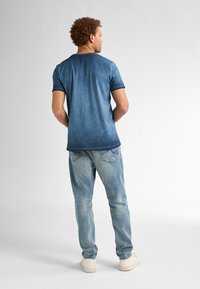 Camiseta de manga corta con degradado azul y cuello redondo, combinada con unos vaqueros de mezclilla azul claro y zapatillas blancas. Textura suave, corte casual.