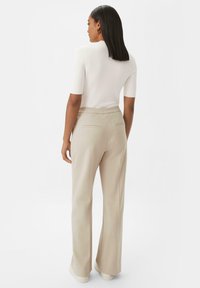 Haut ajusté blanc à manches courtes associé à un pantalon taille haute large beige clair avec poches arrière et coutures minimales.