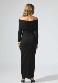 Robe noire à manches longues décolletée, au design près du corps, en tissu texturé, avec une fente dans le dos, agrémentée d'un accent doré sur la manche.