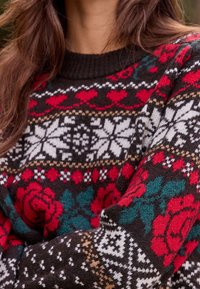 Pull en maille avec une base brun foncé ornée de roses rouges, de flocons de neige blancs et d'accents bleu sarcelle dans un motif Fair Isle. Col côtelé.