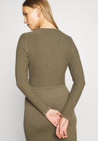 Veste justa de malha verde-oliva com mangas longas, design ajustado e tecido texturizado. Apresenta um decote redondo e um detalhe na cintura.