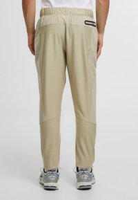 Beżowe spodnie sportowe z elastycznym paskiem w talii i bocznymi kieszeniami. Posiadają teksturowany wzór i kontrastowe przeszycia. Noszone z sportowym obuwiem.