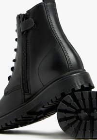 Bottine en cuir noir avec une fermeture éclair sur le côté, conception à lacets, semelle en caoutchouc robuste et semelle texturée pour une meilleure adhérence.