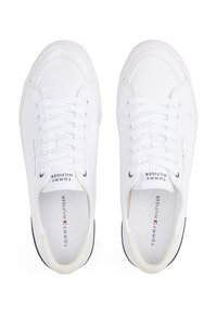 White canvas sneakers with lace-up design, rubber sole, and black accents. "Tommy Hilfiger" branding visible on the tongue and side.