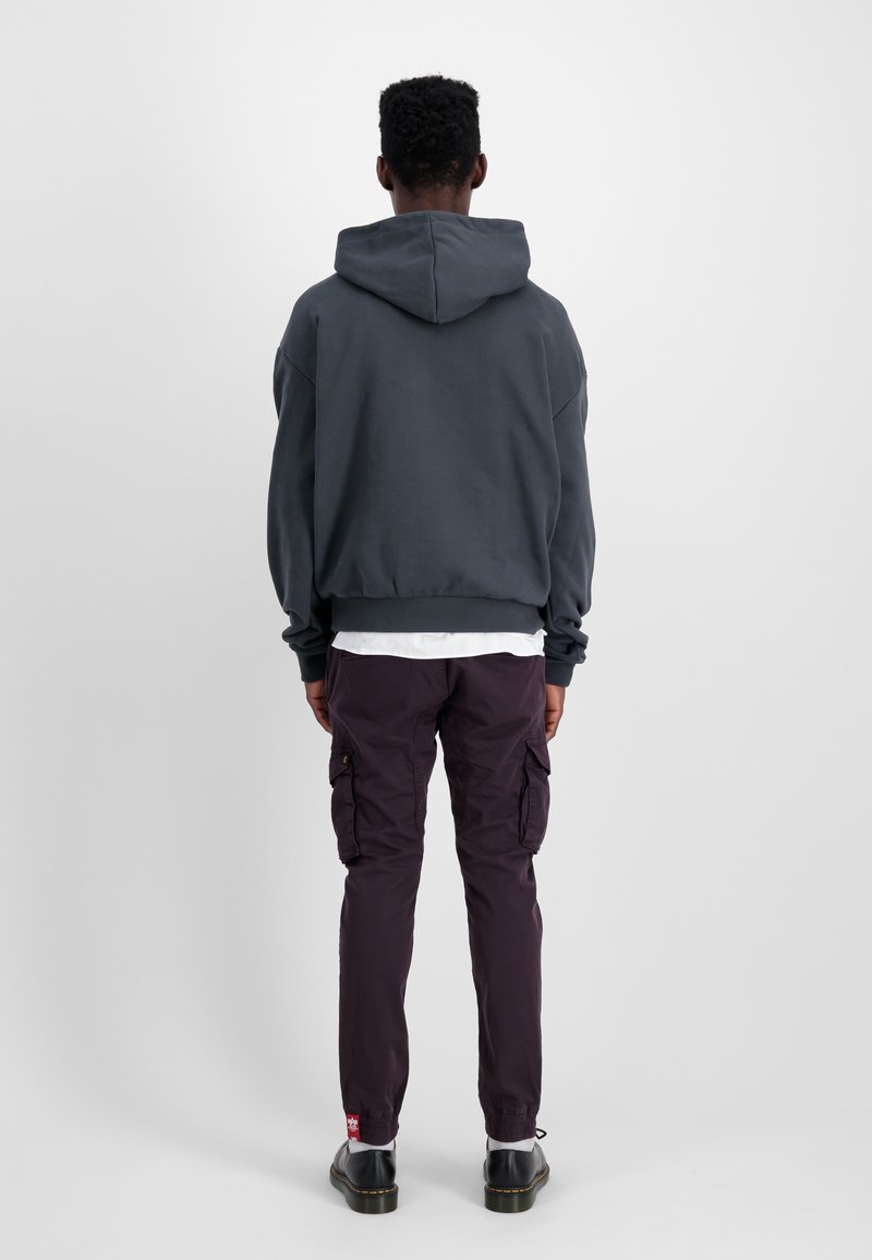 Ciemnoszara bluza z kapturem o luźnym kroju, z prążkowanymi mankietami i dołem. W zestawie z purpurowymi spodniami cargo z bocznymi kieszeniami i naszywką z logo. Czarne buty.