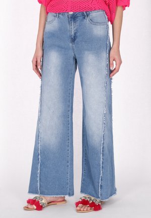Jeans in denim a gamba larga di colore azzurro chiaro con cuciture laterali scaldate. Abbinati a sandali decorati con frange rosse. Top in maglia testurizzata di colore rosa.