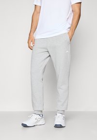 Gray sweatpants in a relaxed fit, made of a soft material, featuring a small white logo on the left thigh, paired with white athletic shoes.