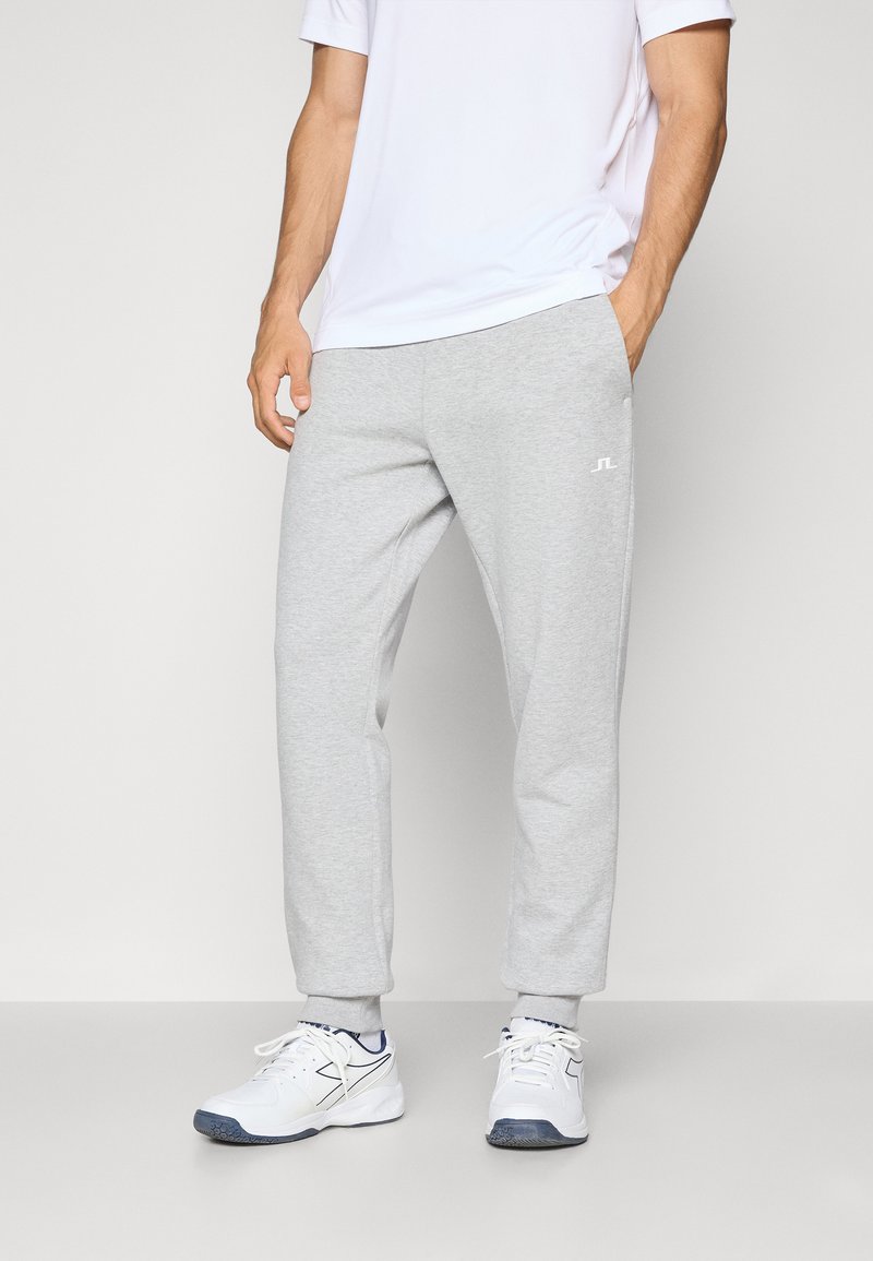 Gray sweatpants in a relaxed fit, made of a soft material, featuring a small white logo on the left thigh, paired with white athletic shoes.