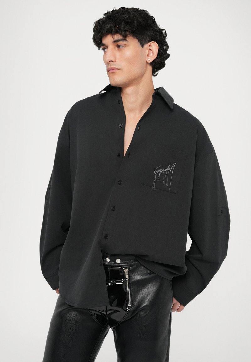 Zwarte blouse met lange mouwen, in een relaxte pasvorm, met knoopsluiting, een oversized kraag en een borstzak aan de linkerkant met geborduurde details.