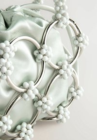 Sac à main en satin menthe avec des ferrures en métal argenté, des accents circulaires et des ornements en perles blanches formant un motif floral.