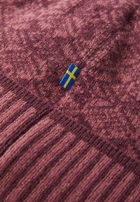 Knitted sweater in deep burgundy with a textured pattern. Features a small blue and yellow Sweden flag label on the side.