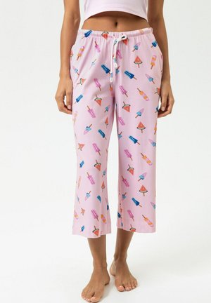 Vrouw draagt roze cropped broek met kleurrijk ijs en watermeloen patroon, staat blootsvoets tegen een witte achtergrond.