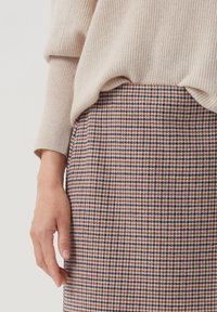 Sukně do délky kolen v multicolor houndstooth vzoru s tkaninou typu tweed. Na vrchu je částečně vidět krémový, žebrovaný svetr.