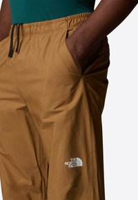 Shorts bruns légers avec une taille élastique, un cordon de serrage et des poches. Présente le logo The North Face en blanc sur la jambe inférieure.