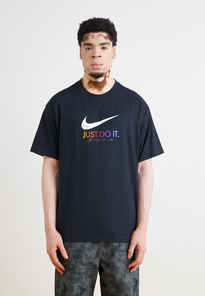 Juodas medvilninis marškinėliai su spalvingu "JUST DO IT." logotipu ir swoosh grafika. Trumpomis rankovėmis, laisvas prigludimas, tekstūruotas audinys.