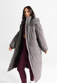 Gepolsterter Steppmantel in einem braun-weißen Karomuster, mit hohem Kragen, großen Ärmeln und einer knöpfbaren Vorderseite.