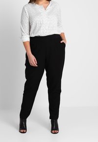 Blouse blanche à motifs avec des manches trois-quarts, associée à un pantalon noir ajusté et des escarpins ouverts noirs. Design simple et décontracté.