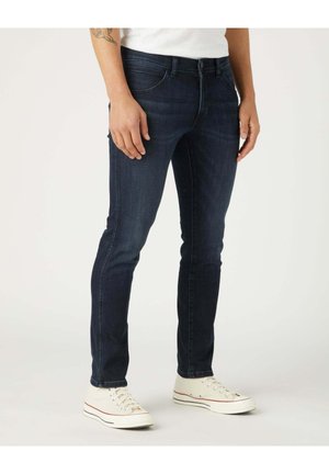 Jeans in denim blu scuro con una vestibilità slim, design a cinque tasche e zip. Abbinati a sneakers in canvas bianco sporco.
