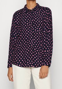 Camicia a maniche lunghe in tessuto blu navy con un motivo di cuori rosa. Presenta un colletto classico e una chiusura con bottoni sul davanti.