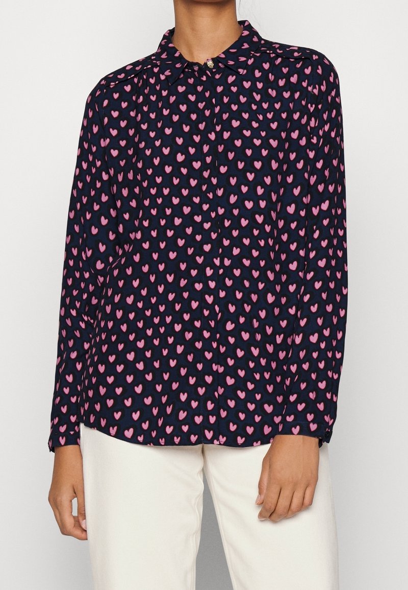 Camicia a maniche lunghe in tessuto blu navy con un motivo di cuori rosa. Presenta un colletto classico e una chiusura con bottoni sul davanti.